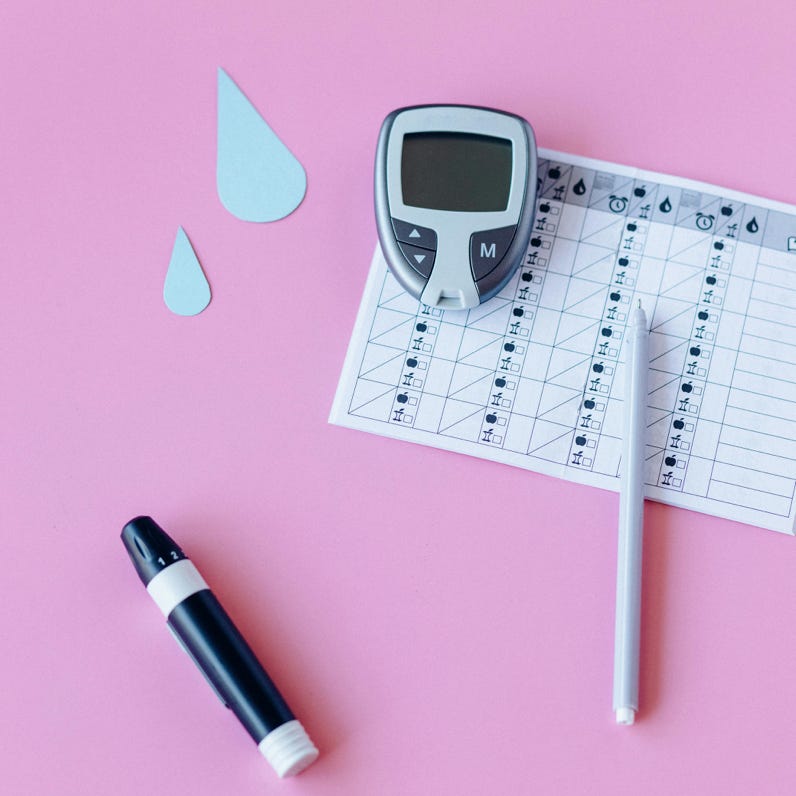 Flat lay of diabetes monitoring tools on a pink background.