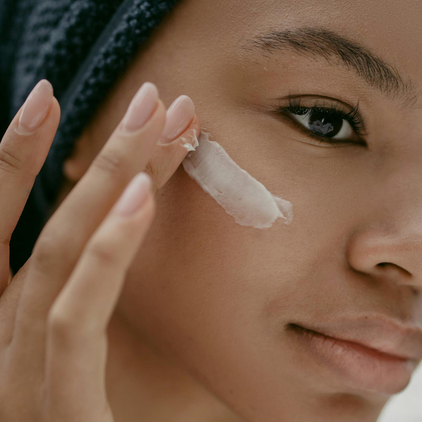 A woman gently applies moisturizing cream to her cheek, promoting healthy skin care.
